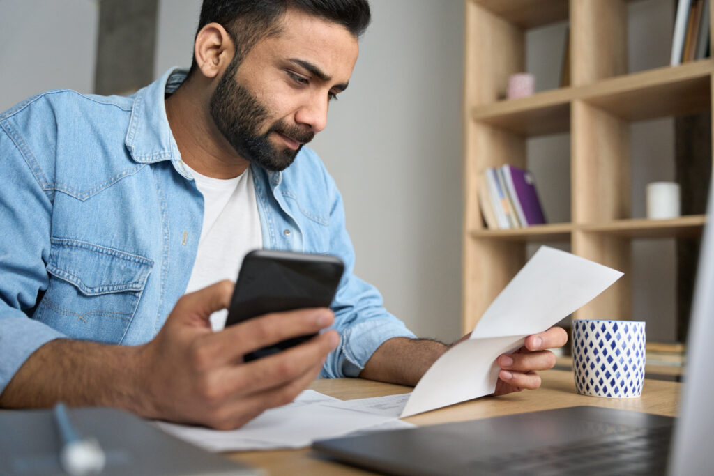 youngindianbusinessmanholdingphonereadingbankreceiptcalculatingtaxes